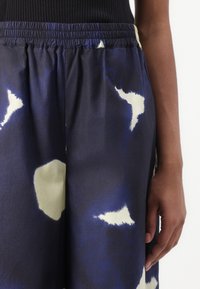 Multicolored pants featuring a blue and cream abstract pattern, lightweight fabric, elastic waistband, and a relaxed fit.