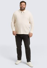 Hellbeiges Langarm-Poloshirt mit einem Drei-Knopf-Kragen, kombiniert mit dunklen Jeans und weißen Sneakers. Glatte Textur und schlichtes Design.