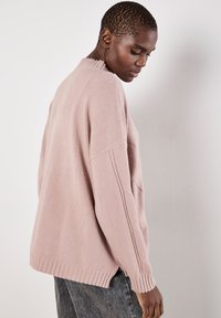 Helles rosa, übergroßes Sweatshirt mit geripptem Kragen und Saum, mit überschnittenen Schultern und strukturiertem Strickmuster. Weiches, kuscheliges Material.