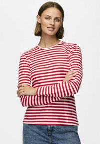 Röd och vit randig långärmad skjorta med rund krage, ribbad textur och figurnära design. Kombinerad med blå jeans.