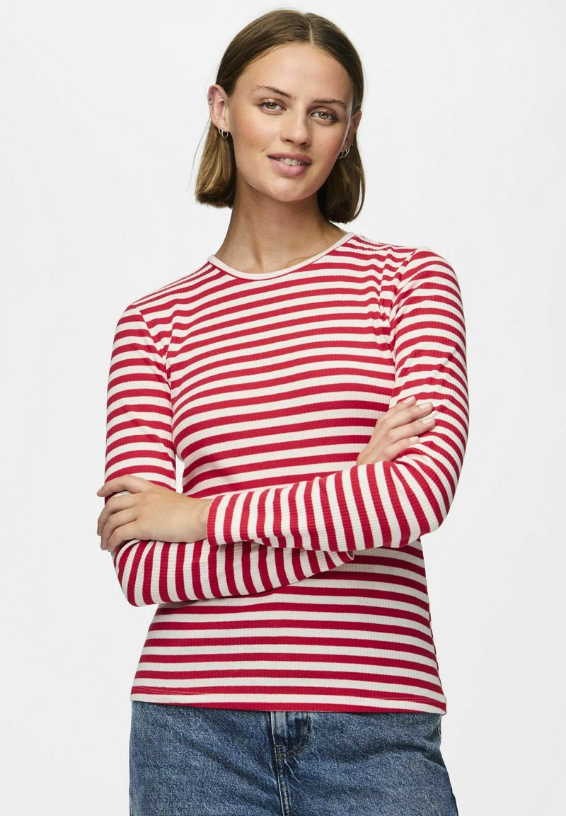 Röd och vit randig långärmad skjorta med rund krage, ribbad textur och figurnära design. Kombinerad med blå jeans.