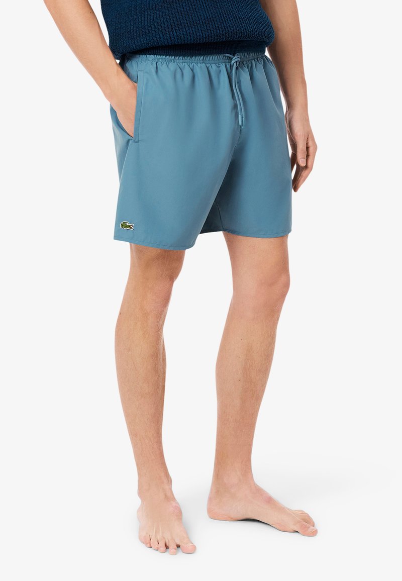 Pantaloni da nuoto blu realizzati in tessuto leggero, con vita elastica dotata di coulisse, tasche laterali e un piccolo logo Lacoste.