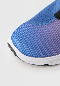 But sportowy z teksturowaną, niebiesko-fioletową siateczką na cholewce, białą podeszwą środkową oraz czarną gumową podeszwą zewnętrzną, charakteryzujący się smukłym designem.