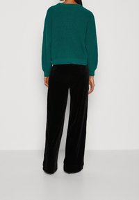 Dzianinowy sweter w kolorze morskim o szerokim kroju z prążkowanymi detalami, zestawiony z czarnymi, welurowymi spodniami o szerokich nogawkach. Oba elementy mają teksturowane wykończenie.