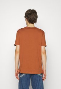 Rostfarbenes Baumwoll-T-Shirt mit kurzen Ärmeln, Rundhalsausschnitt und geradem Schnitt, von hinten präsentiert und mit einer glatten Textur.