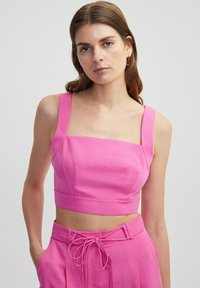 Fitted, square-neck crop top in bright pink fabric with wide straps and seam detailing, paired with matching high-waisted trousers.