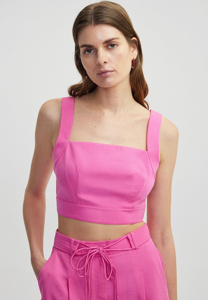 Fitted, square-neck crop top in bright pink fabric with wide straps and seam detailing, paired with matching high-waisted trousers.