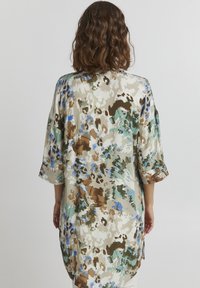 Lös passform i lätt tyg med ett abstrakt mönster av grönt, blått, brunt och beige. Har trekvartsärmar och rundad nederkant.