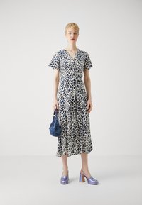 Abito midi in stampa leopardata bianca e blu, con maniche corte e cintura in vita. Abbinato a una borsa a tracolla blu testurizzata e scarpe con tacco lilla.