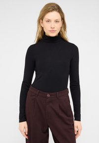 Czarny golf z długim rękawem z prążkowanej tkaniny, zestawiony z wysokim stanem bordowych spodni z zapięciem na guziki i teksturowaną tkaniną.