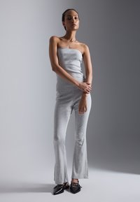 Grå, ribbet, stroppeløs jumpsuit med flagrende ben, kombineret med spidse sorte sko med dekorative detaljer. Glat tekstur, tætsiddende design.