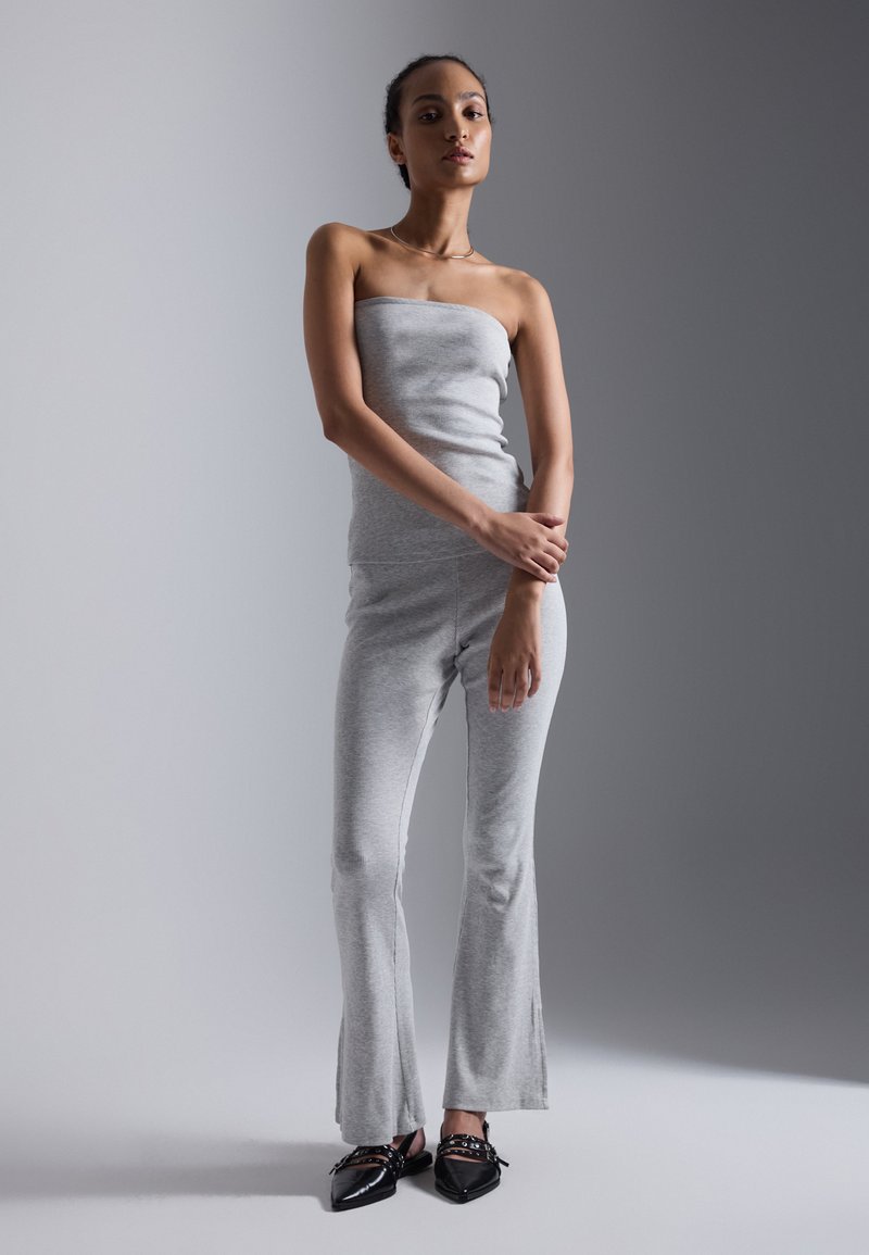 Grå, ribbet, stroppeløs jumpsuit med flagrende ben, kombineret med spidse sorte sko med dekorative detaljer. Glat tekstur, tætsiddende design.