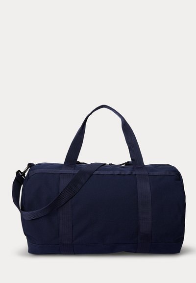 Τσάντα duffel σε ναυτικό μπλε χρώμα με διπλές επάνω λαβές και ρυθμιζόμενο ιμάντα ώμου σε απλό ανοιχτό φόντο.