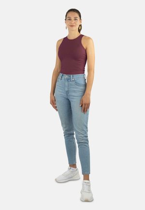 Bordeaux-farbenes ärmelloses Top kombiniert mit hellblauen hoch-taillierten Skinny Jeans und weißen Sneakers, mit einem figurbetonten Design und glatter Textur.