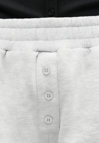 Κοντινό πλάνο ανοιχτόχρωμου γκρι φόρμας με ελαστική μέση και τρία κάθετα κουμπιά στο μπροστινό μέρος, συνδυασμένη με μαύρο ριπ τοπ.