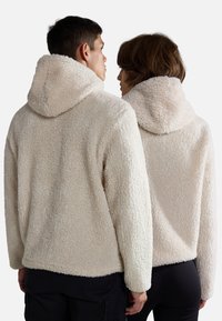 Felpe con cappuccio in morbido pile di colore crema chiaro, con una superficie testurizzata, dotate di cappucci e spalle scese, viste da dietro.