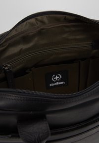 Sort lædertaske med olivengrønt stoffor, har lynlåslomme, organiseringssektioner og Strellson-mærke.