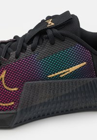 Sort atletiksko med en tekstureret mesh-overdel med et gradientmønster i lilla, blågrøn og pink. Indeholder et guldaccentslogo.