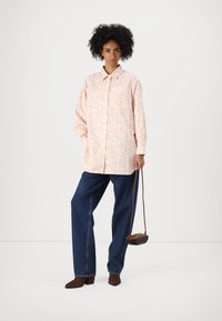 Chaqueta de camisa rosa de manga larga con un patrón floral, combinada con unos vaqueros oscuros de corte holgado y botas de tacón marrones, sosteniendo un pequeño bolso marrón.