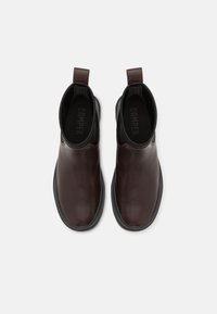 Paire de bottines en cuir marron foncé à enfiler, semelles noires et languettes, vue de dessus sur un fond clair.