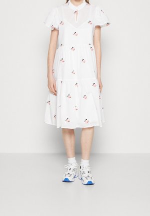 Persoon draagt een witte midijurk met een klein bloemenpatroon, pofmouwen en witte sneakers met blauwe accenten.