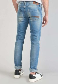 Lichtblauwe denimjeans met een slim fit, voorzien van vervaagde gebieden, achterzakken en opgerolde manchetten, gecombineerd met zwart-witte sneakers.