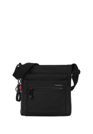 Sort crossbody-taske med justerbar skulderrem, forreste lynlåslomme, lille Hedgren-logo og fastgjort nøglering med rødt accent.