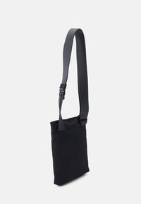 Schwarze Schultertasche aus Stoff mit glatter Textur, verstellbarem Trageriemen, rechteckiger Form und minimalistischem Design.