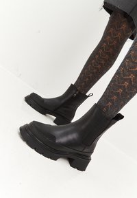 Bottines noires avec une finition en cuir lisse, des accents texturés sur l'orteil, une semelle épaisse et une fermeture éclair sur le côté pour un enfilage facile.