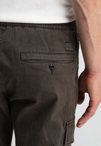 Donkergroene cargoshorts met een gladde textuur, voorzien van een achterzak met knoopsluiting en een klein logo-opdruk op de tailleband.