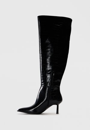 Knöchehohe schwarze Stiefel mit einer glänzenden Krokodilprägung. Spitz zulaufende Zehen und dünner Absatz; mit einem seitlichen Reißverschluss zum Verschließen.