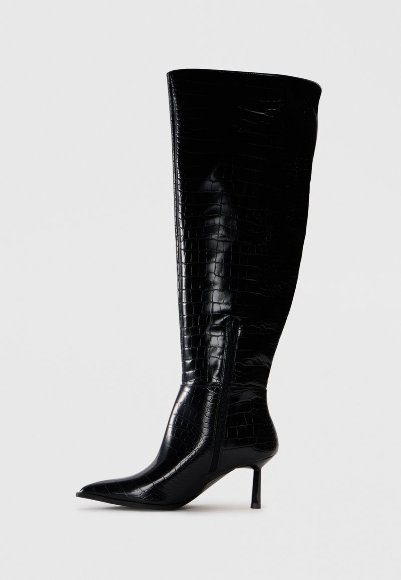 Knöchehohe schwarze Stiefel mit einer glänzenden Krokodilprägung. Spitz zulaufende Zehen und dünner Absatz; mit einem seitlichen Reißverschluss zum Verschließen.