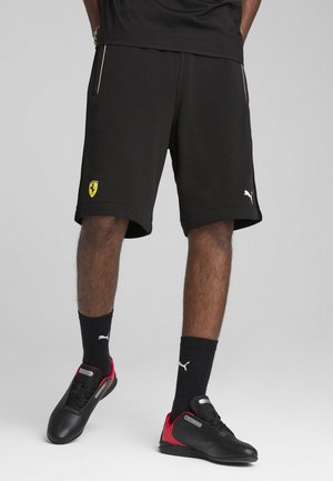 Pantalones cortos deportivos negros con un logo amarillo de Ferrari y un logo blanco de Puma. Llevados con calcetines negros y zapatos negros con acentos rojos.