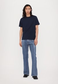 Tricou din bumbac de culoare albastru marin, cu guler rotund, asortat cu blugi din denim deschis la culoare, evazați. Design simplu, cu o croială lejeră.
