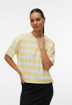 Tumejuustega naine, kes kannab kollase-valge triibulise lühikeste varrukatega särgi ja musta seelikut, poseerib ühe käega taljel.