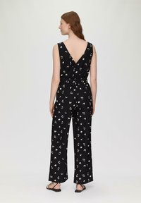 Mono negro con espalda en V, diseño de pierna ancha y patrones abstractos blancos. Presenta una cintura ajustada con una lazada y tirantes finos.
