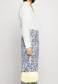 Yellow patent handbag with a crocodile texture, curved shape, and short strap, held alongside a blue and white leopard print skirt and white blouse.