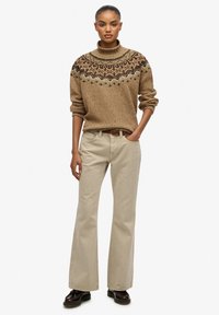 Suéter marrón con patrón y cuello alto, combinado con pantalones beige de campana y zapatos oscuros. El suéter presenta diseños de punto intrincados.