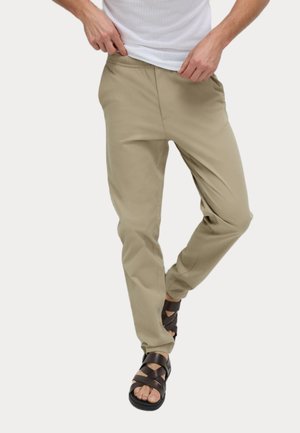 Pantalones ligeros beige con un corte relajado y cintura elástica, combinados con sandalias marrones de tira, que presentan una suela texturizada.