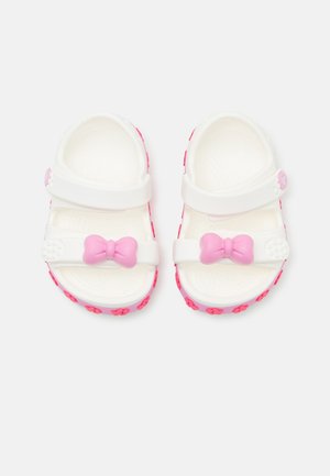 Witte sandalen met roze accenten, voorzien van een strikdetail en bloemenpatronen op de zool. Gemaakt van een flexibel, lichtgewicht materiaal.