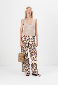 Top in beige, pantaloni palazzo a fantasia in crema, bordeaux e navy, con una borsa circolare intrecciata. Sandali semplici completano l'outfit.