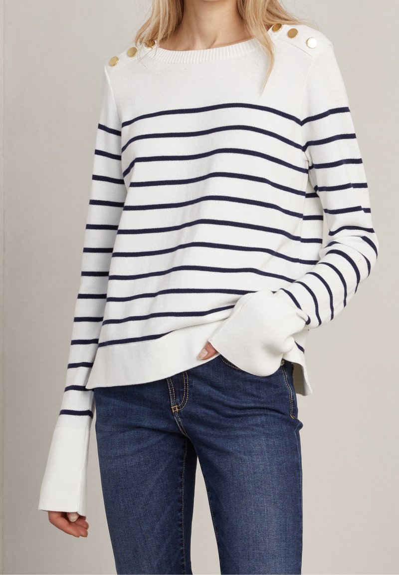 Vit randig tröja med mörkblå horisontella ränder, med knappar på axlarna, ribbad halsringning och avslappnad passform. Kombineras med mörk jeans.