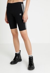 Black cycling shorts with white side stripes and Adidas logo, paired with black lace-up boots and white ankle socks. Smooth textile finish.