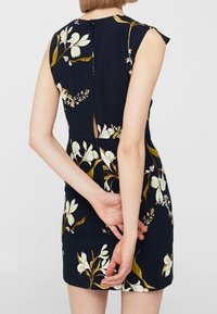 Robe bleu foncé avec motifs floraux blancs et jaunes, manches courtes, silhouette ajustée et ouverture en forme de trou de serrure à l'arrière.