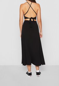 Černé maxi šaty s uzávěrem na zadní straně a kříženými ramínky; lehká tkanina a délka k kotníkům; v kombinaci s černými teniskami.