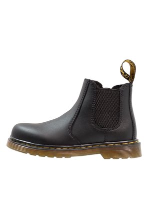 Botín Chelsea negro hecho de cuero suave con paneles elásticos laterales, costuras amarillas y una suela de goma texturizada.