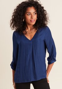 Blusa leggera di colore blu navy con scollatura a V e maniche a tre quarti. Presenta una texture morbida e una leggera lucentezza con una vestibilità rilassata.