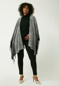 Sciarpa con stampa leopardata nera e grigia con bordi frangiati, abbinata a un dolcevita nero e pantaloni neri aderenti, che mettono in evidenza forme e texture eleganti.