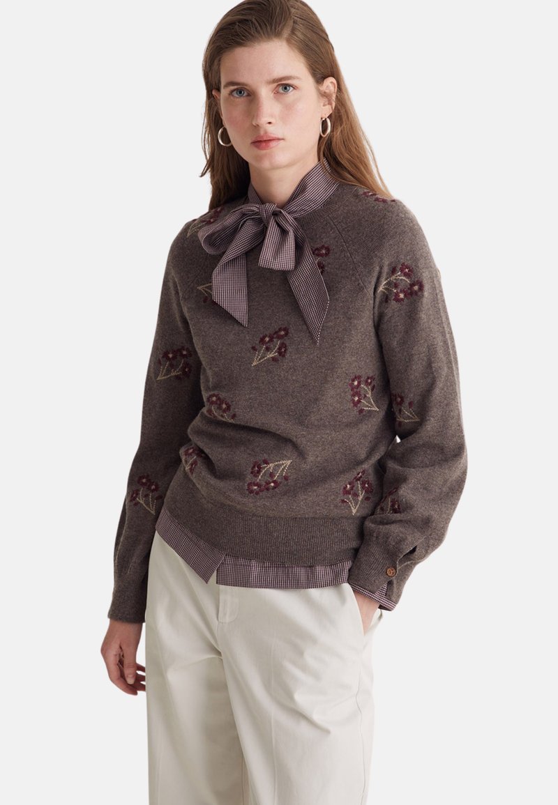 Maglione marrone in misto lana con ricamo floreale. Presenta un collo a fiocco in tessuto a quadri e un effetto a più strati con un orlo a righe.