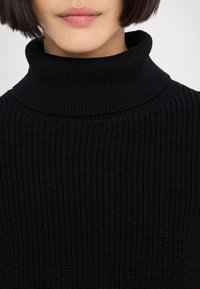 Schwarzer gerippter Rollkragenpullover mit hohem Kragen, strukturiertem Strickstoff und tailliertem Design, der Wärme und Komfort betont.